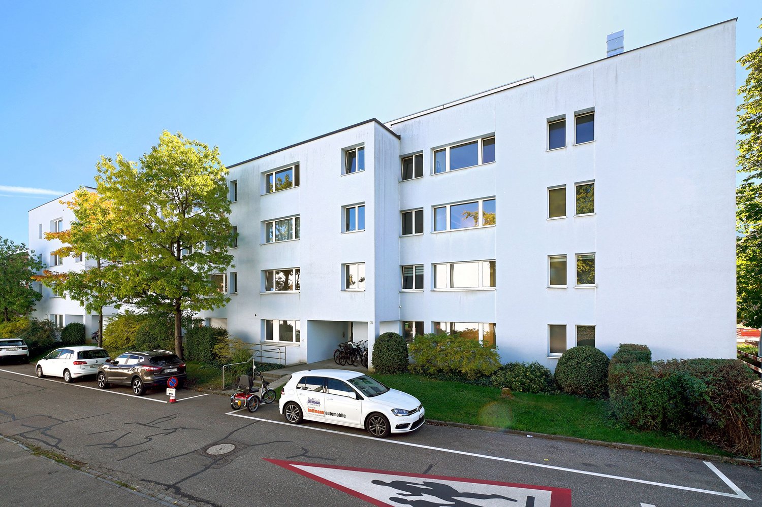 Apartment building, multi-story, white, parking spaces in front of the building