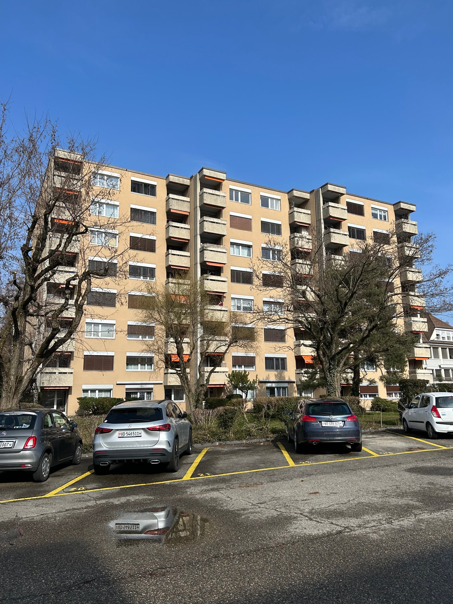 Multi-story apartment building with balconies, parking spaces in the front