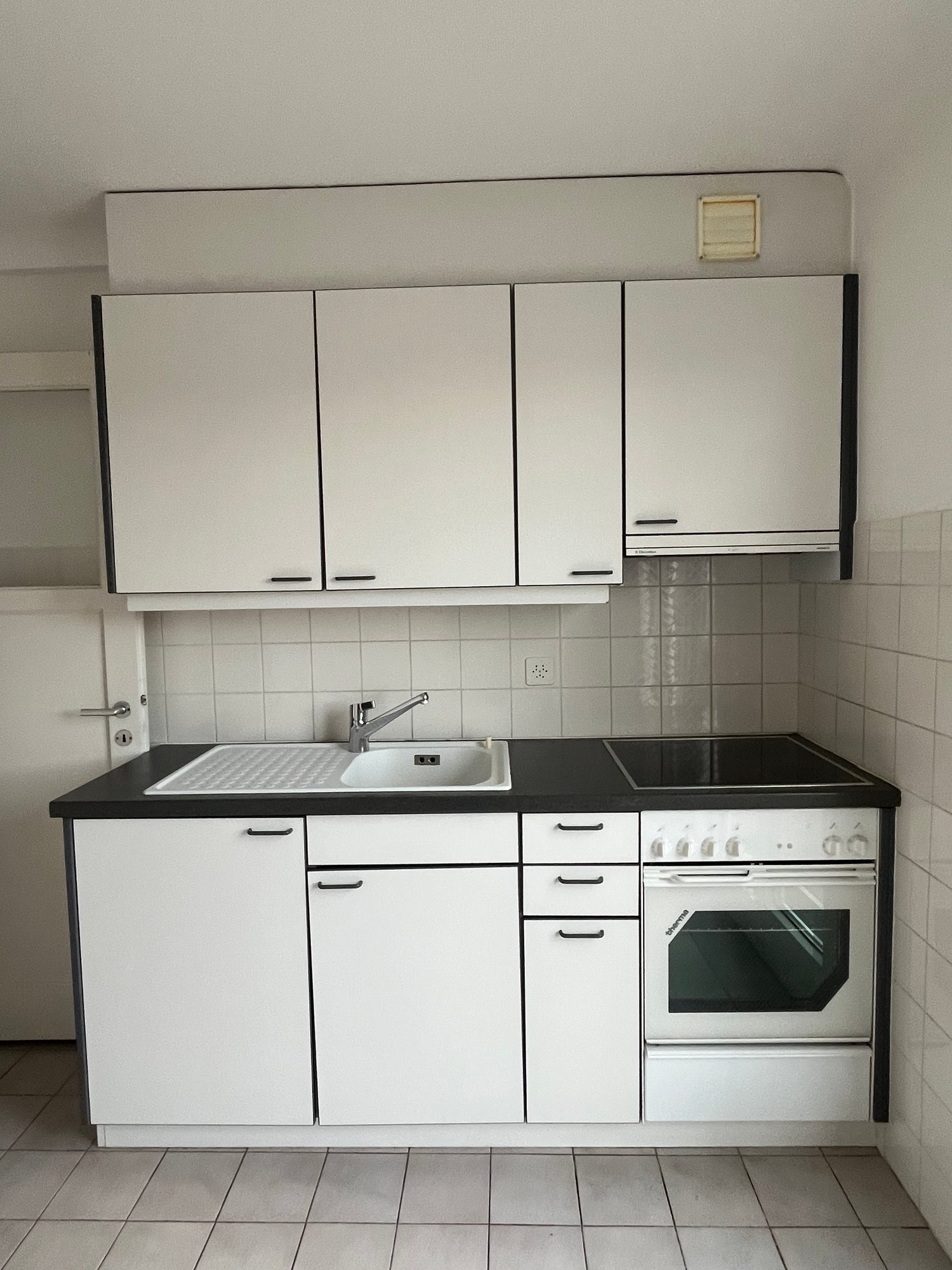 modern fitted kitchen with white cabinetry and black countertops, white oven, stainless steel sink and faucet, dishwasher, tiled floor