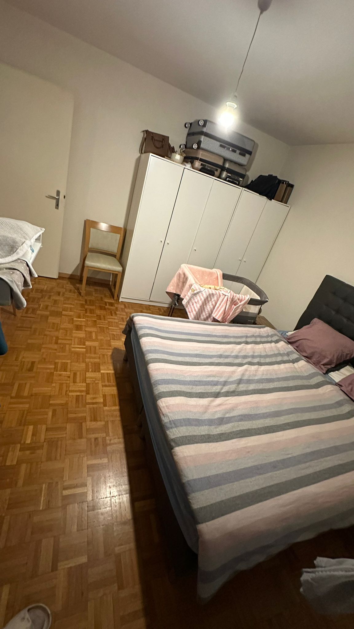 bedroom with two beds, one chair, and wardrobe, wooden floor, white walls, light lamp