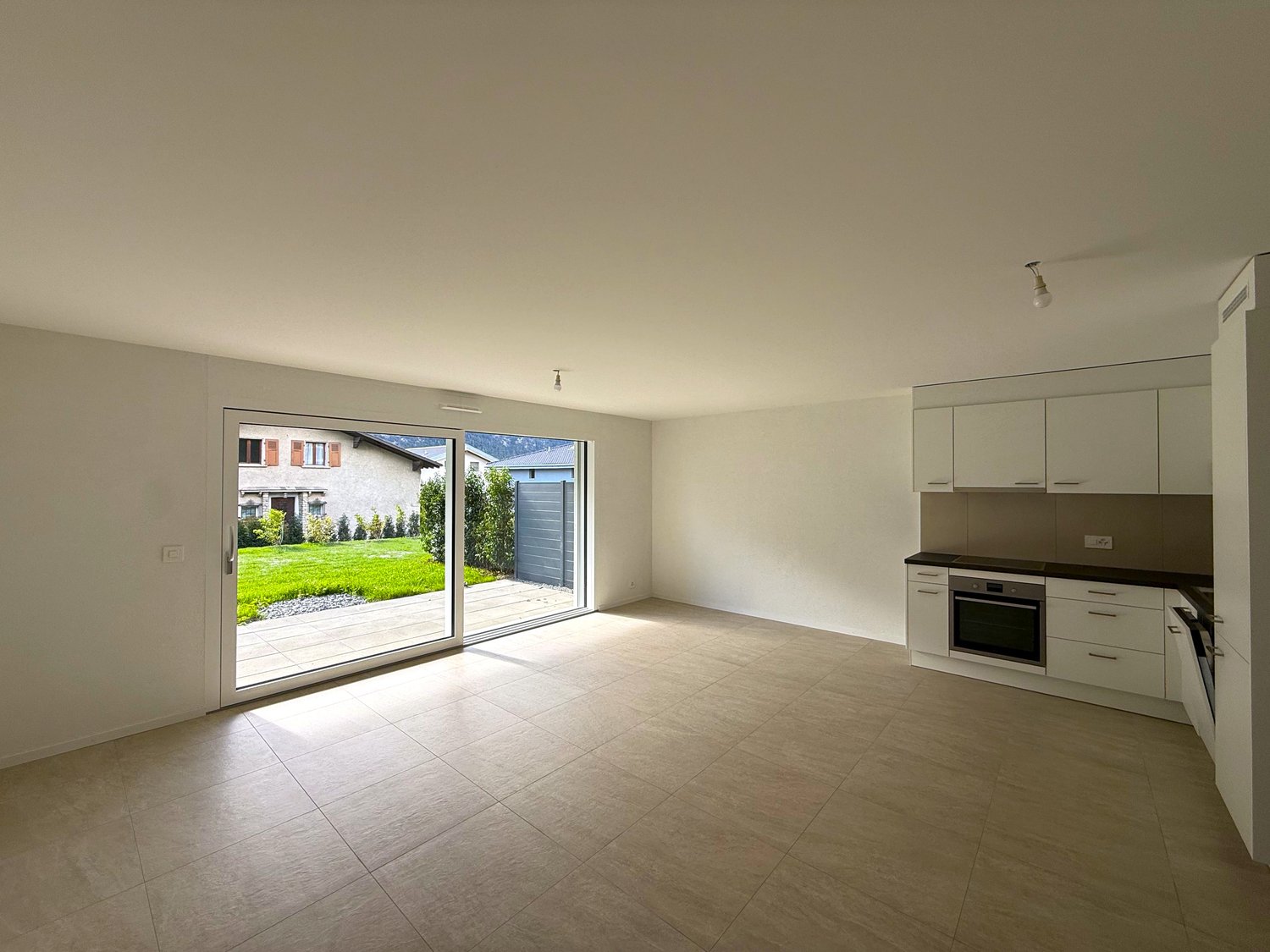 large sliding glass door, modern kitchen with integrated appliances, tiled floor, open to outdoor patio
