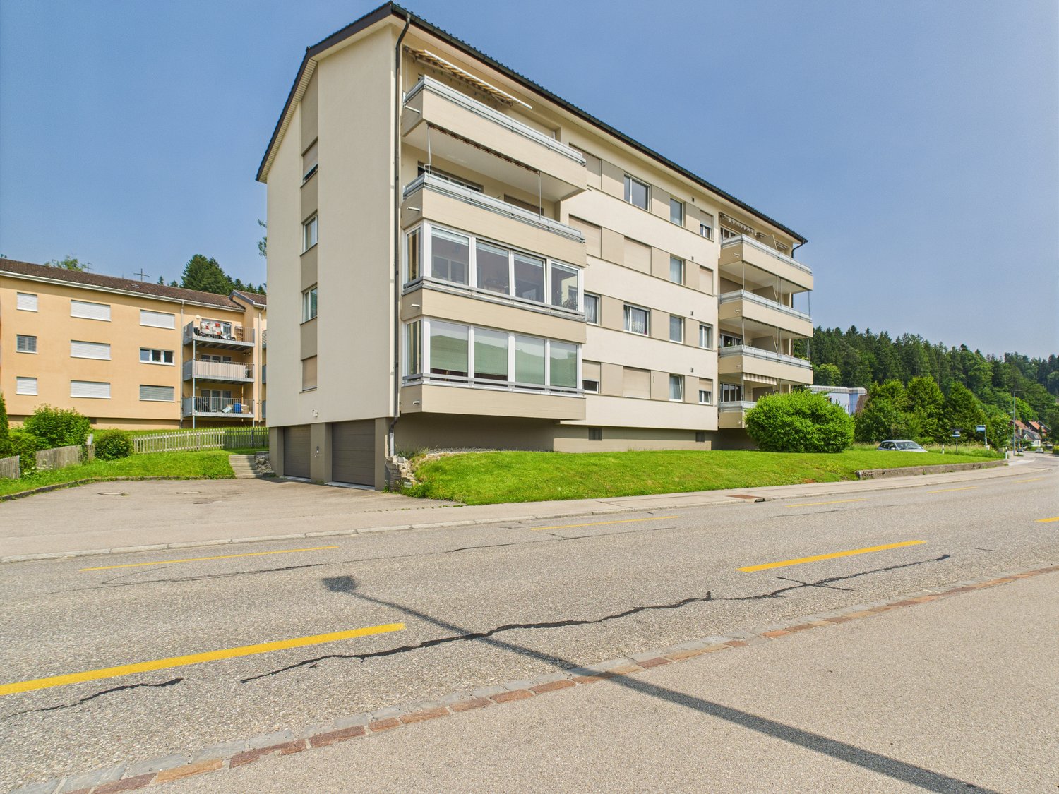 4-story apartment building, beige exterior, balconies, surrounded by greenery and trees