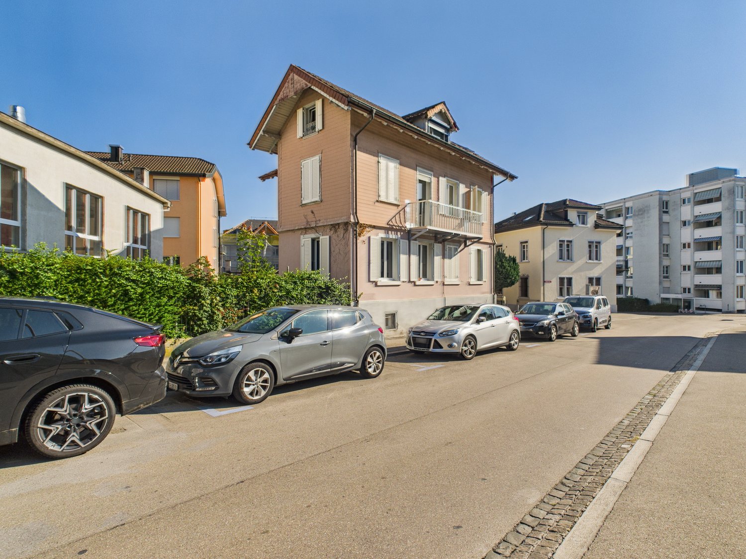 Multiple houses and buildings, street with cars parked, balconies visible on the middle building