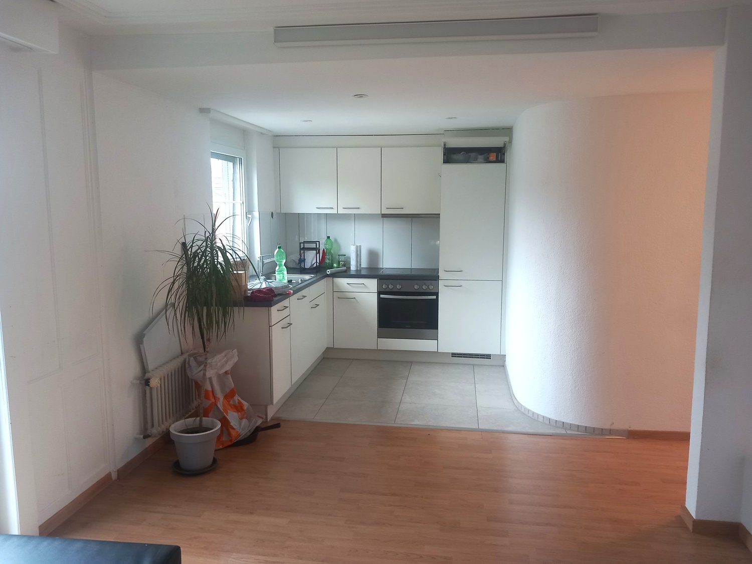 White cabinets, tiled floor, black countertops, potted plant, sink, oven, refrigerator, and lamps mounted on the ceiling.