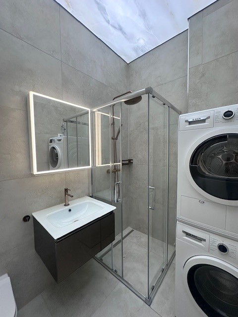modern design bathroom with a shower, white sink, dark cabinet, washing machine, and a toilet