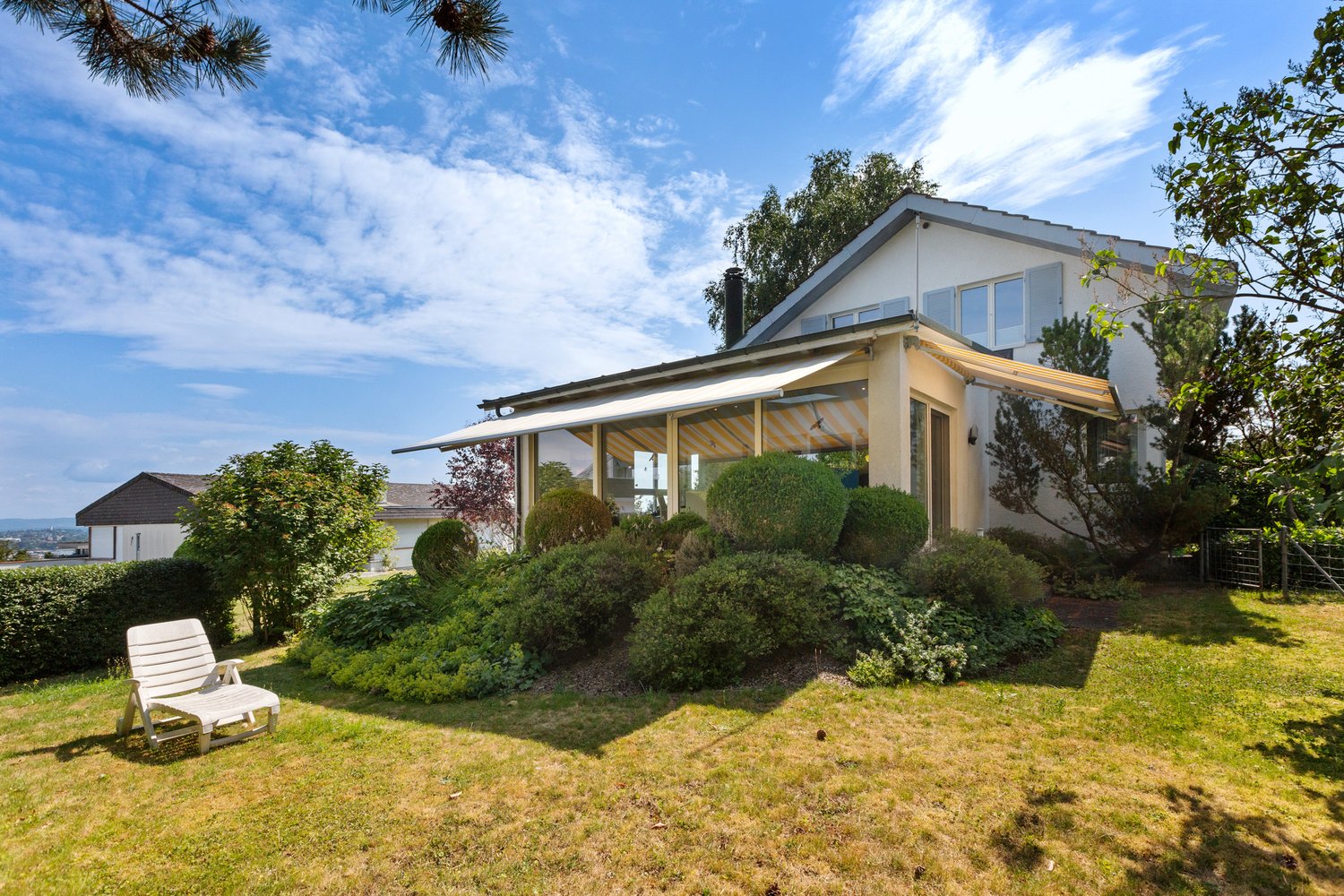 Single-family house, white exterior, beige awnings, large garden with bushes and a lawn