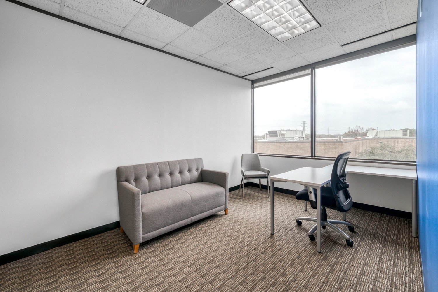an empty room with a couch, desk, and two chairs, with windows to the outside