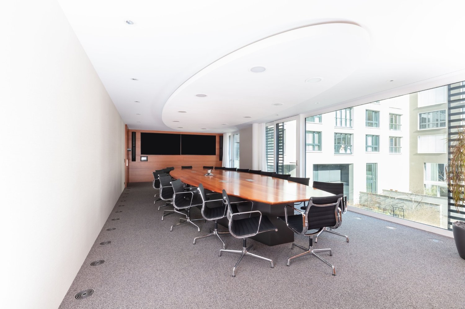 modern office meeting room, large wooden table, grey carpet, glass walls, built-in monitors