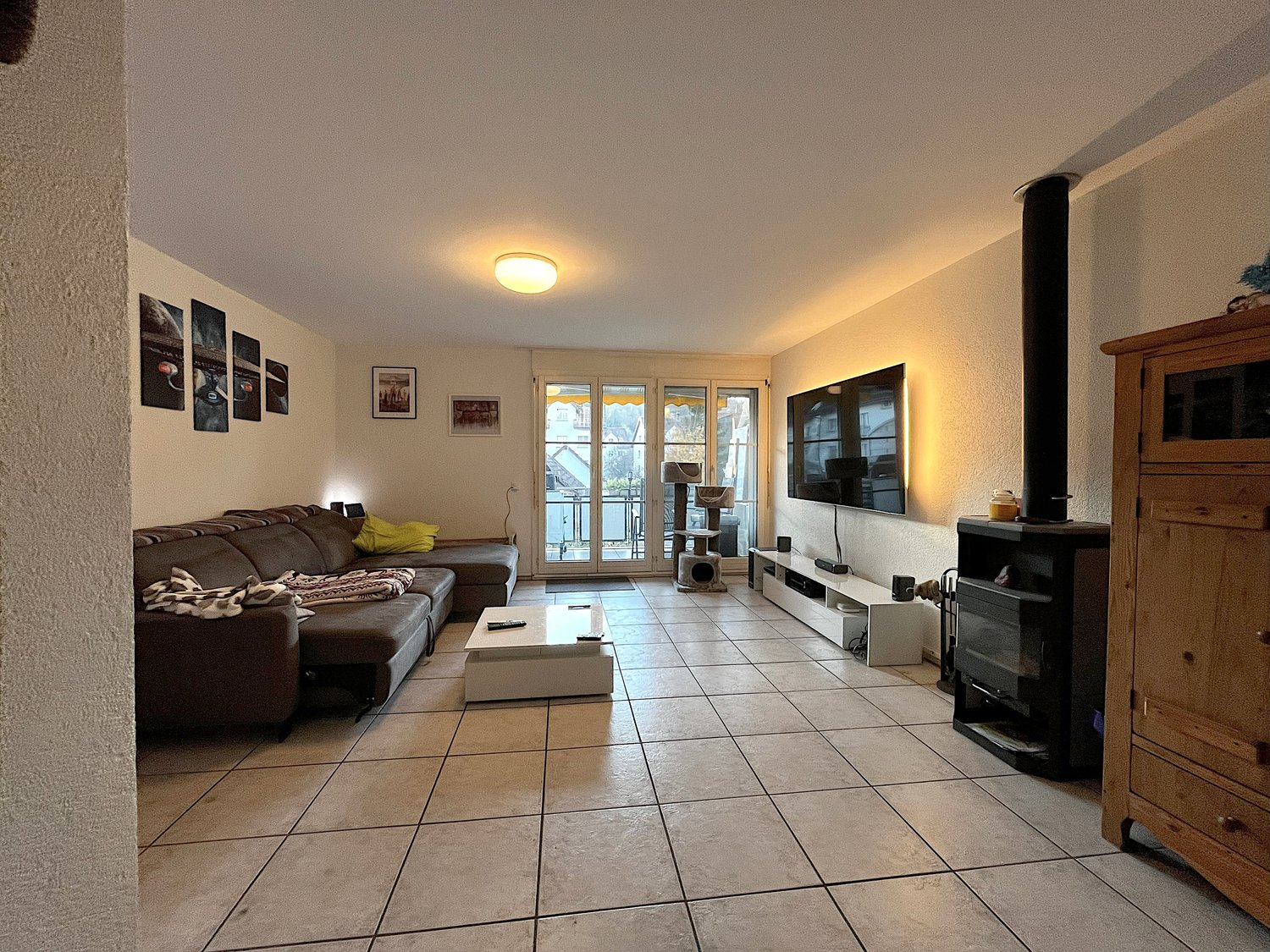 wooden couch, TV mounted on wall, fireplace, center table, entertainment cabinet, tiled floor, sliding glass doors