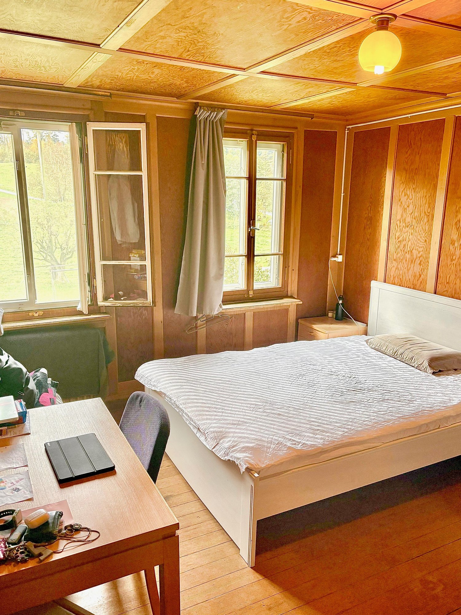 spacious bedroom with wooden floor, bed, desk, radiator, 2 windows, curtains
