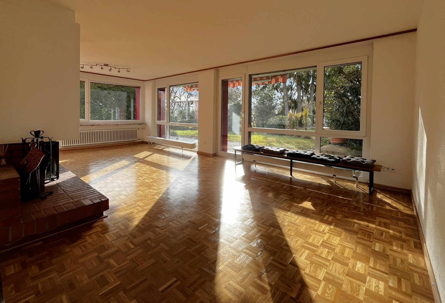 large room, wooden floor, glass walls, fireplace, bench, natural light, windows