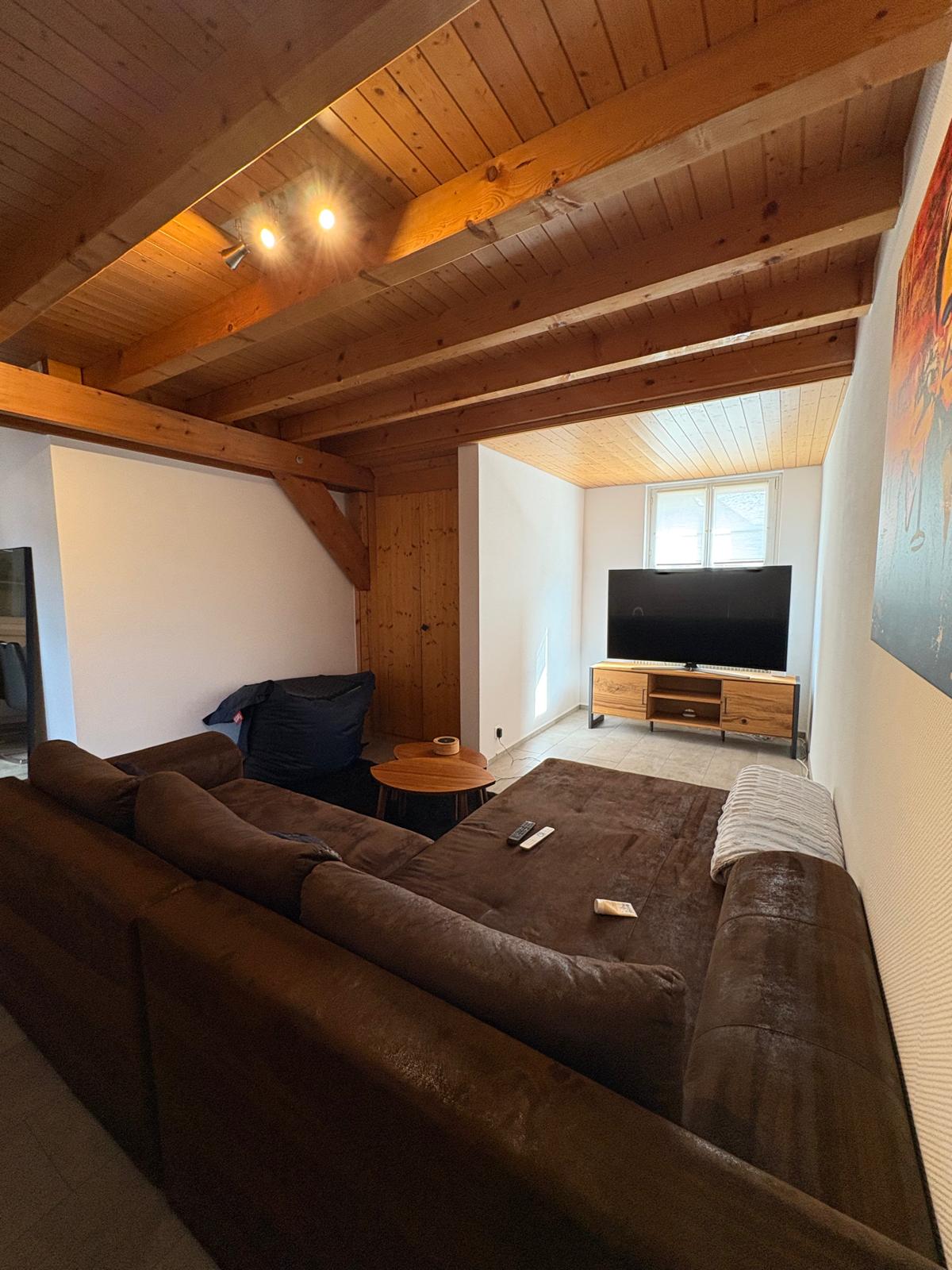 L-shaped couch, TV with media stand, round coffee table, wooden beams