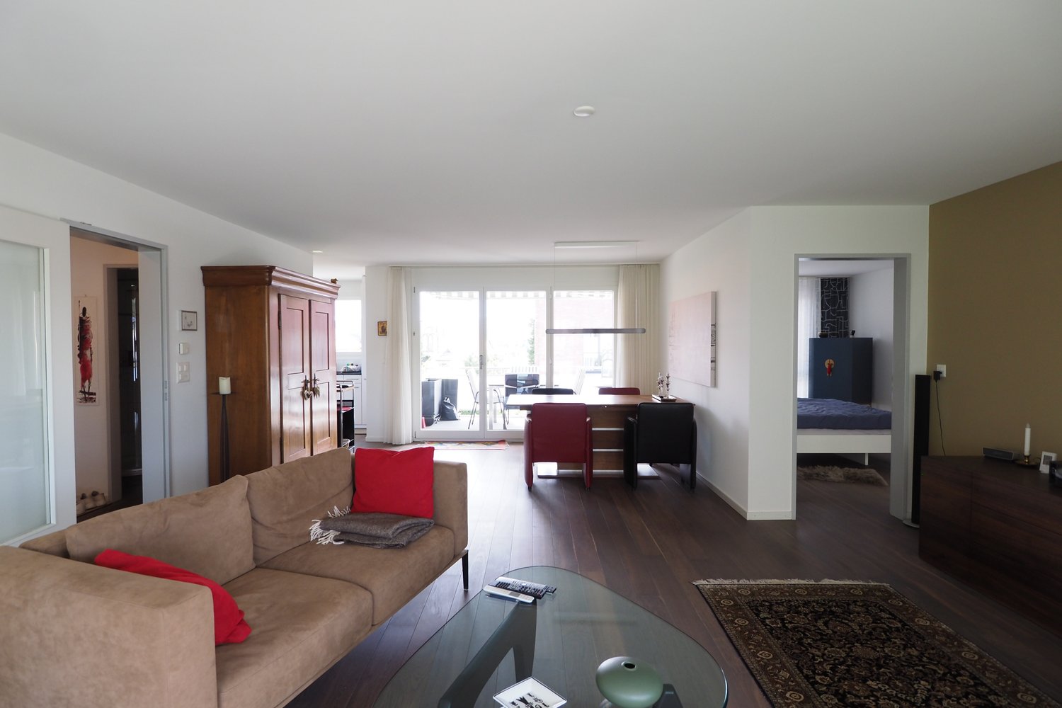 Living room with couch, table, rug, open windows, wooden flooring, side cabinet, dining table with chairs