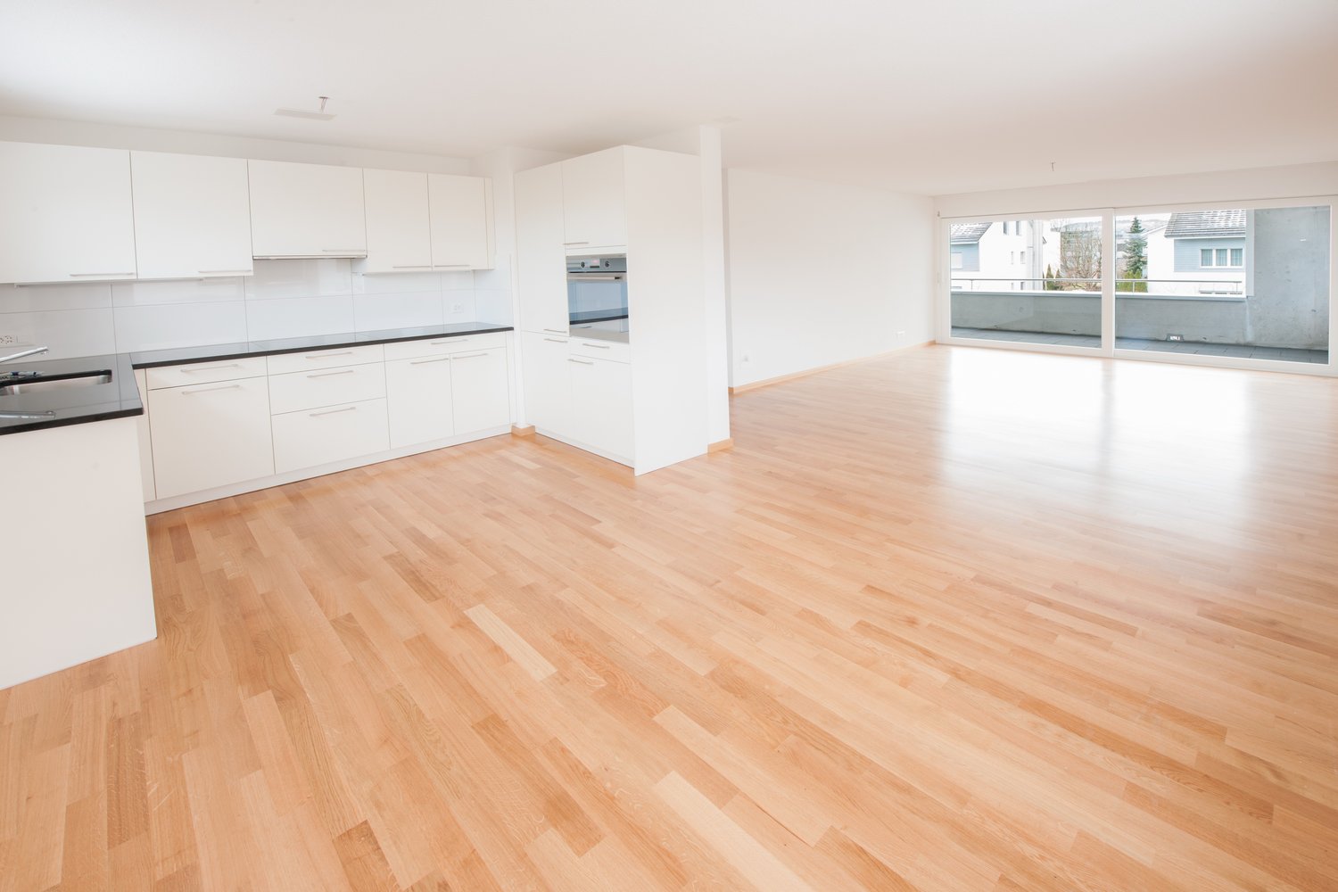 modern kitchen with wooden floors, black granite countertops, white cabinets, double sink, built-in oven, balcony, sliding glass doors