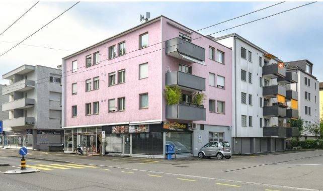 Multi-story building, pink facade, several balconies, storefront at ground floor