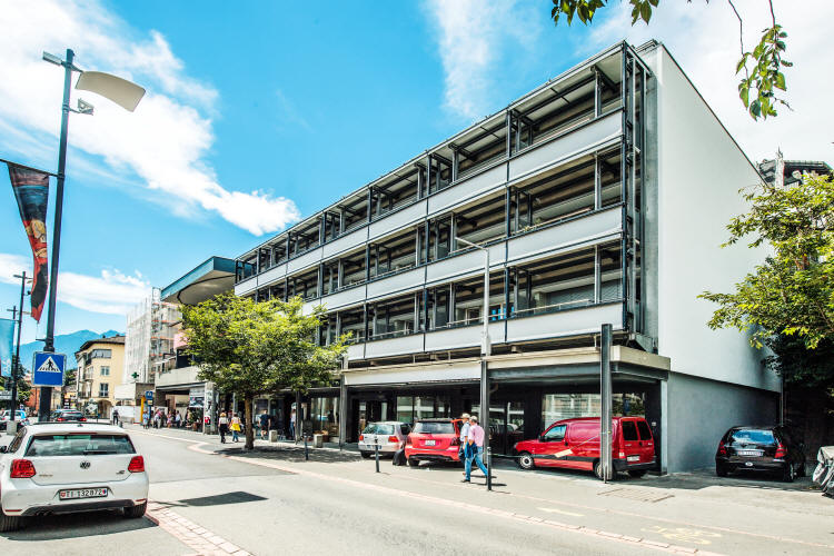 multi-story building, white exterior, multiple windows, cars parked in front, street with cars and pedestrians