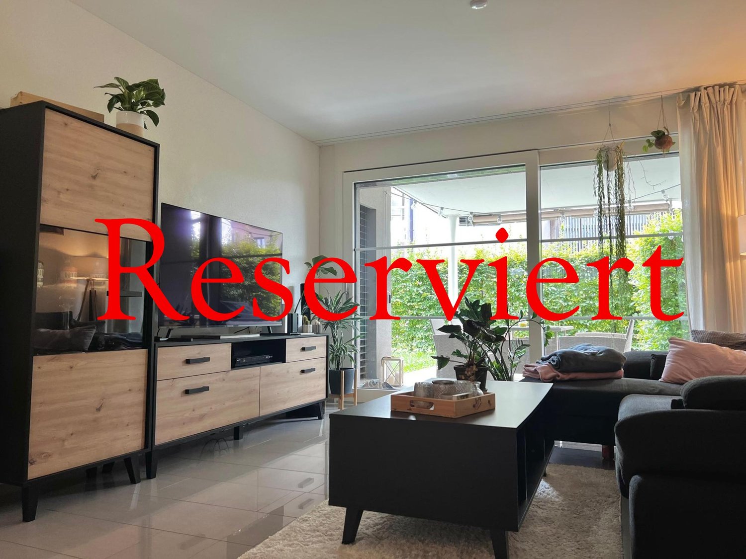 Contemporary living room with a sofa, a television set, and an open space leading to a balcony with outdoor furniture.