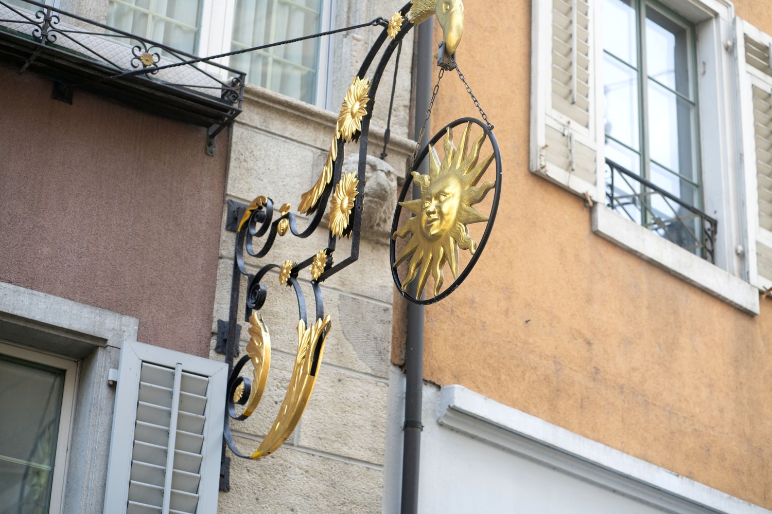 Black and gold decorative sign with a sun emblem hanging from a building.