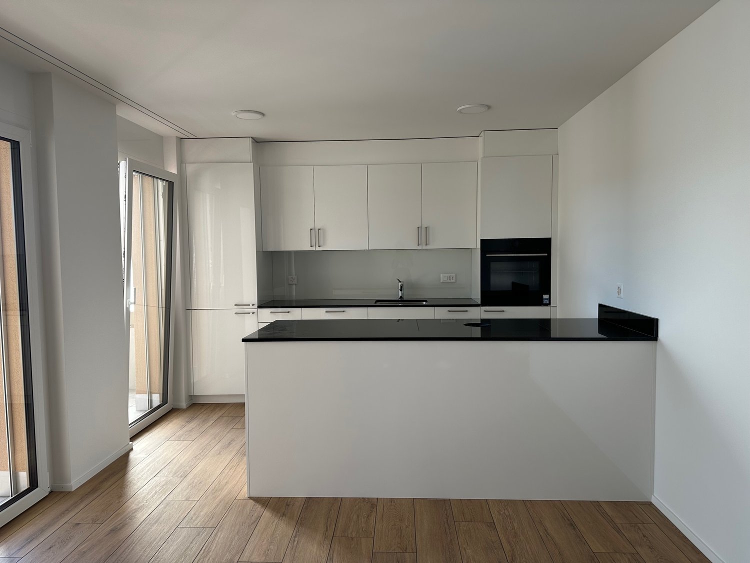 modern kitchen with white cabinets, black countertop, integrated oven, and sliding glass doors