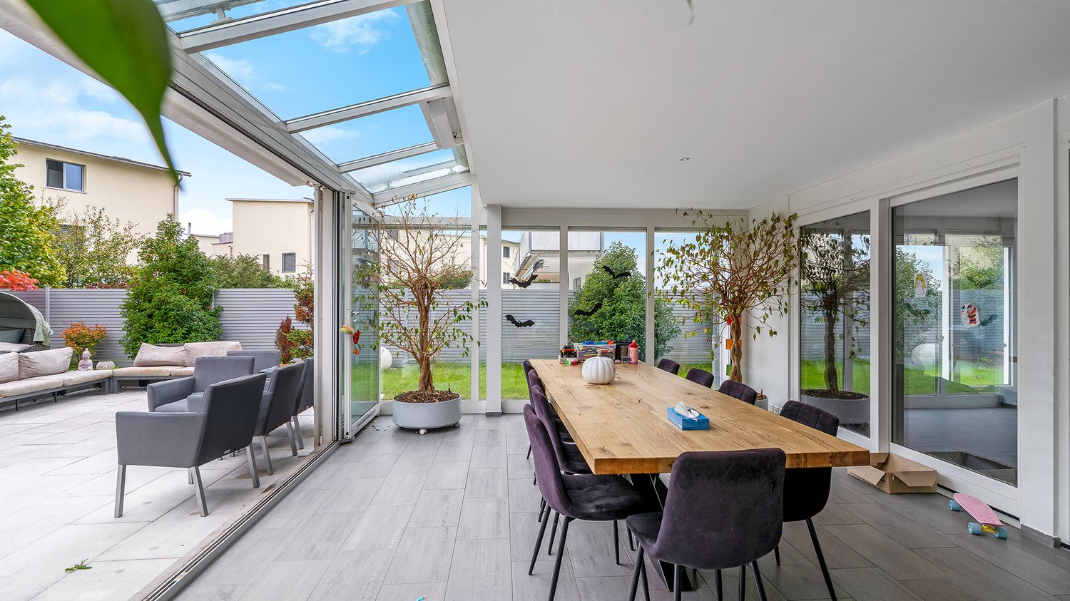 long table, many chairs, two potted trees, sliding glass door