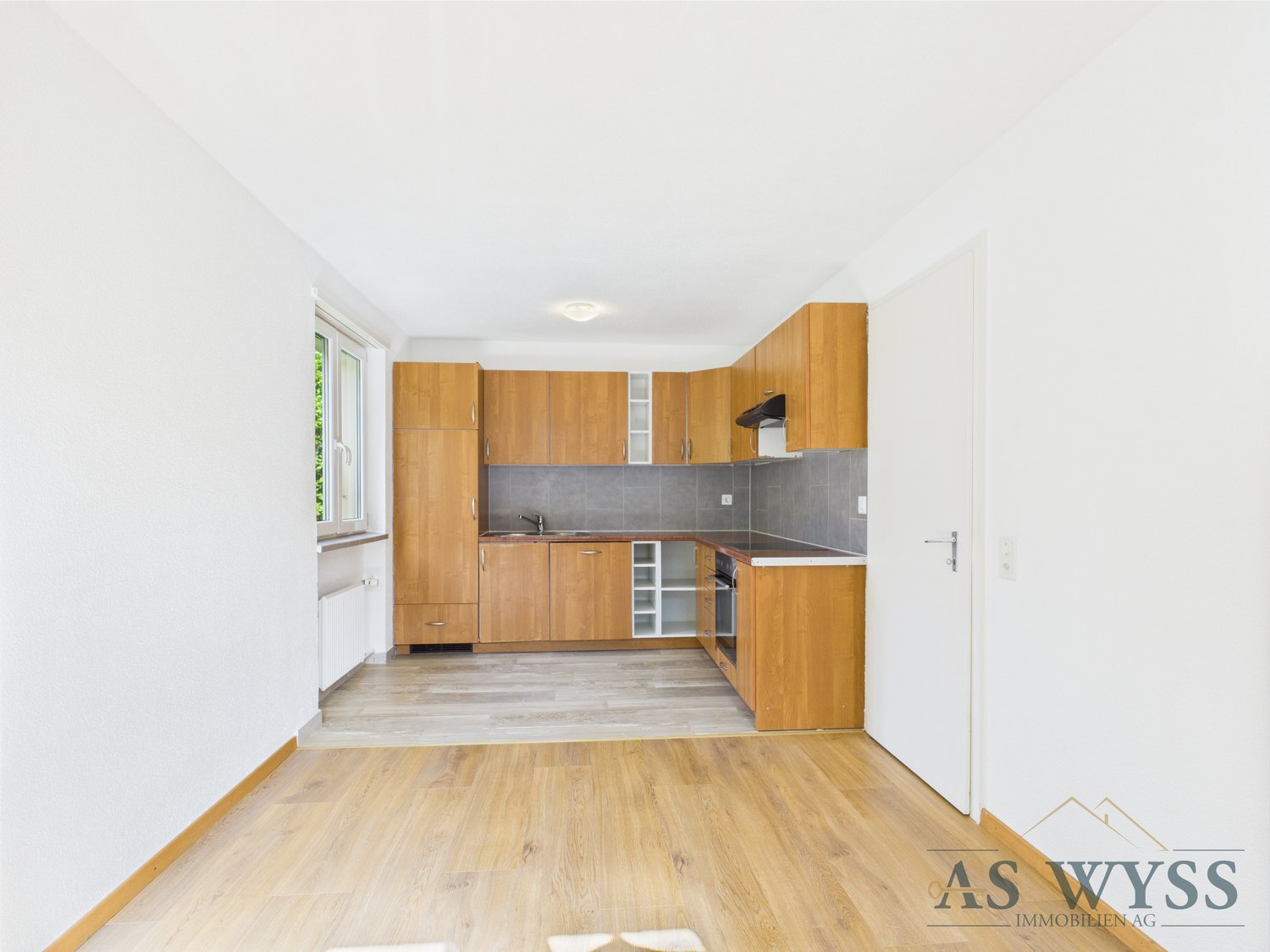 Empty room with white walls, wooden cabinets, countertop with kitchen, window, radiator