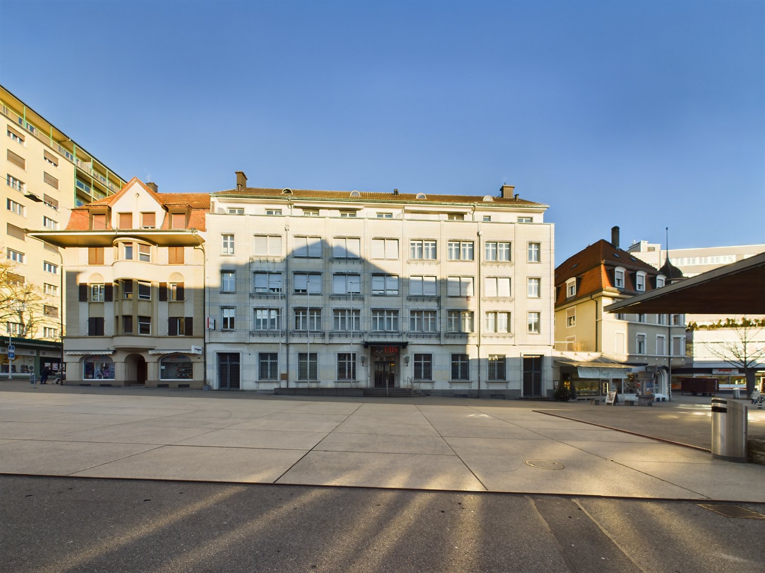 Urban building, 3 floors, multiple windows, large paved area in front