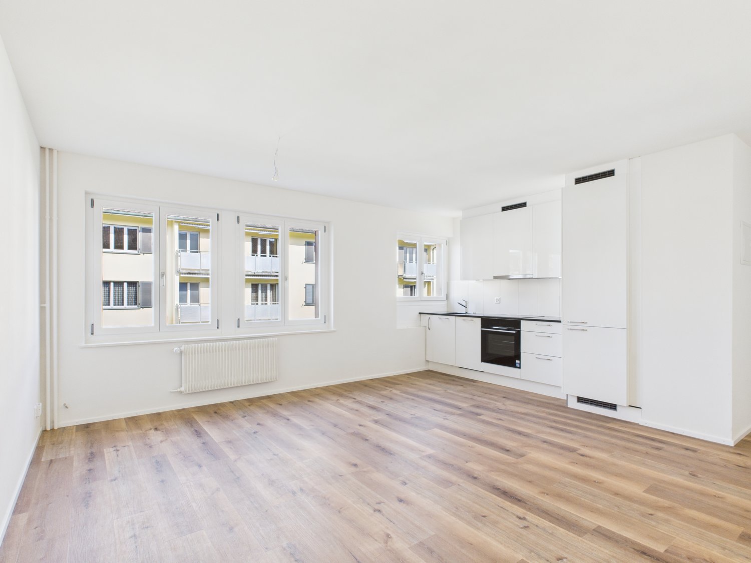 Open kitchen with large windows, wooden floor, white cabinets, modern black oven and sink