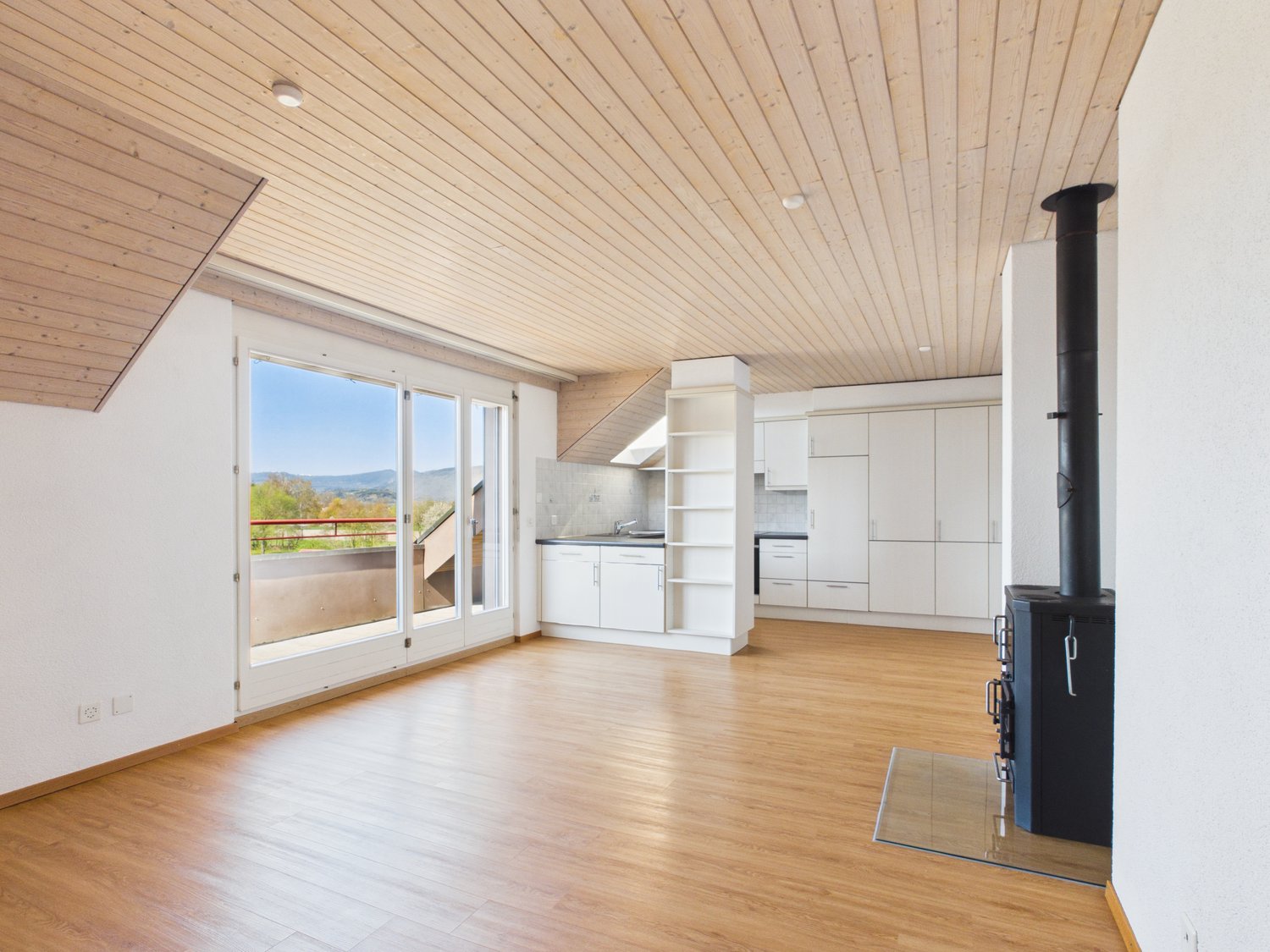 wooden floor, white walls, large windows, balcony, fireplace, kitchen with white cabinets