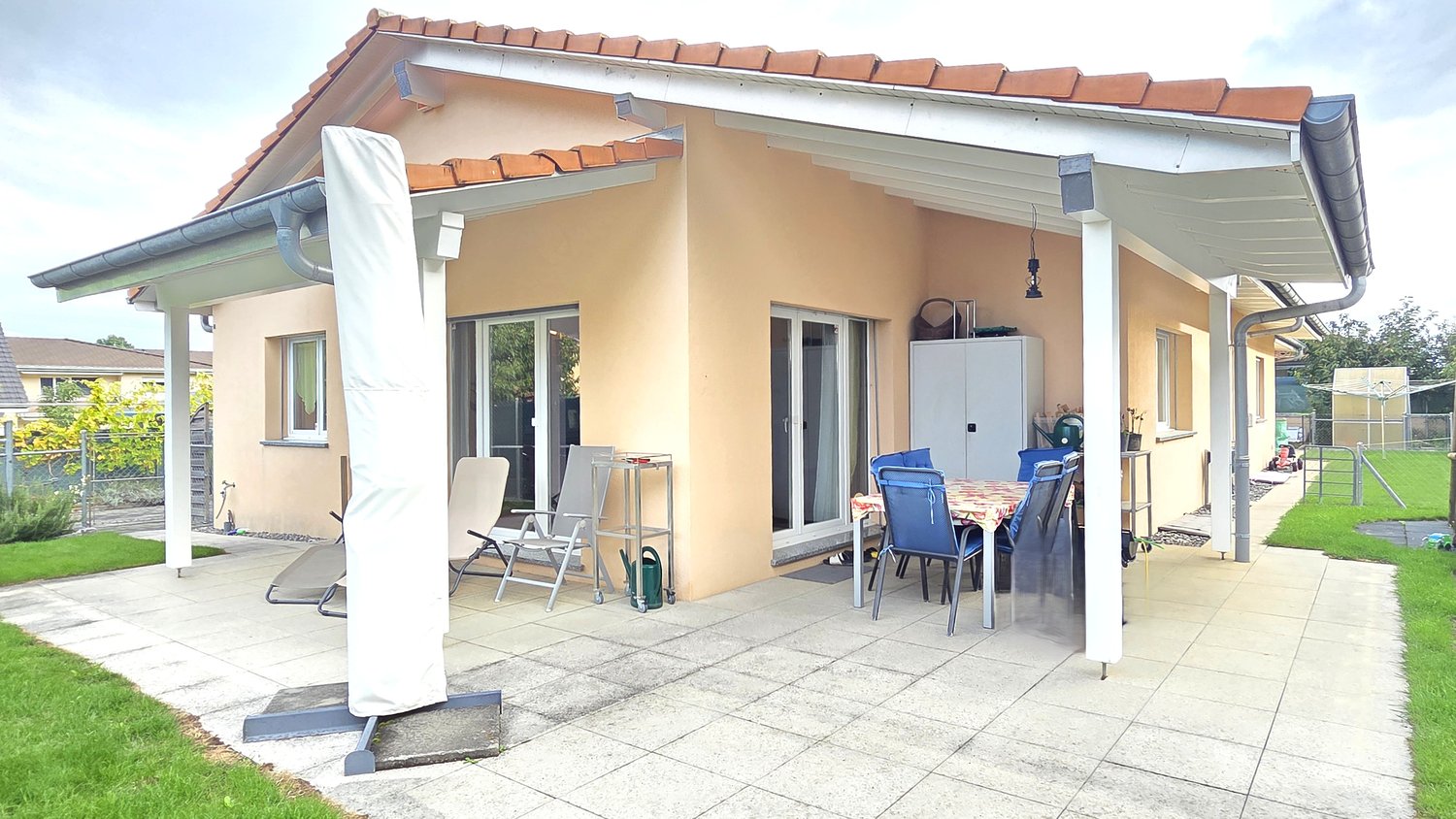 Single story house, red tiles roof, terrace, covered by awning, table, chairs, patio, garden, lawn, shrubs