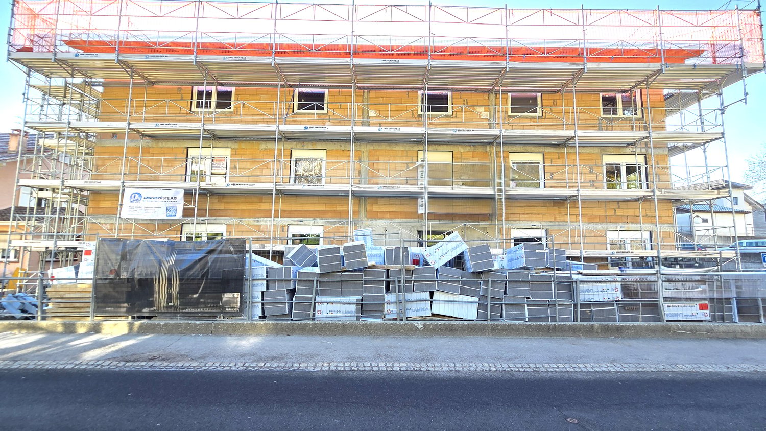 Building under construction, scaffolding, multiple windows, materials stacked in front