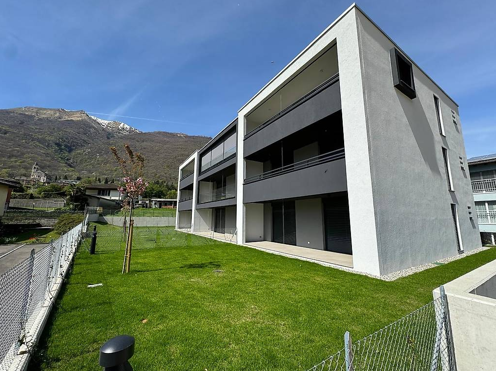 3-story modern apartment building with large windows, balconies, and a grassy lawn in front surrounded by a fence