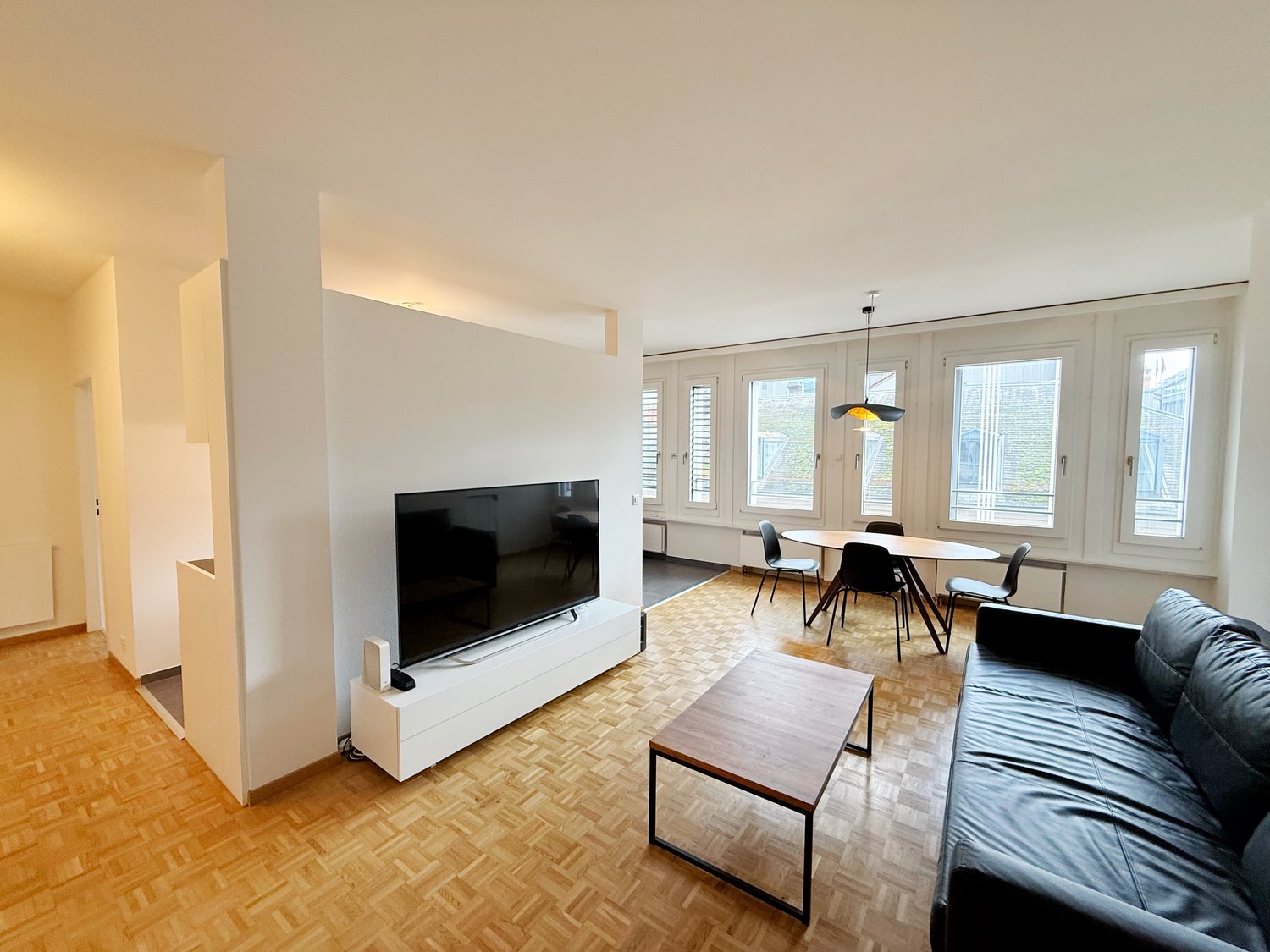 modern apartment, large windows, parquet floor, couch, TV, coffee table, dining table with chairs, wooden table