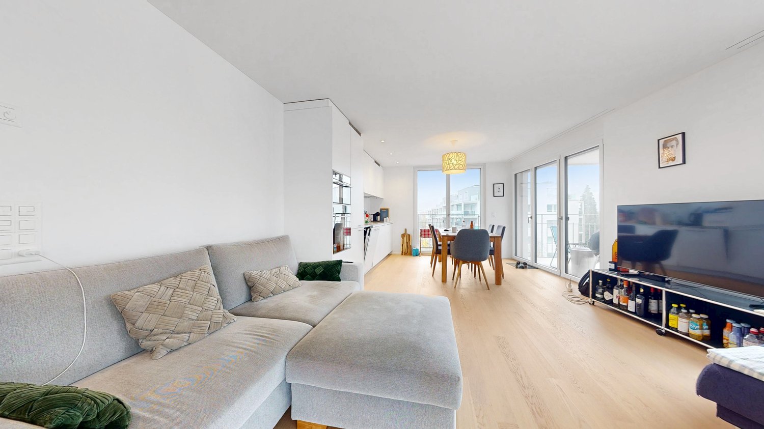 contemporary style living room, gray couch, dining table, flat screen TV, wooden floors, open floor plan