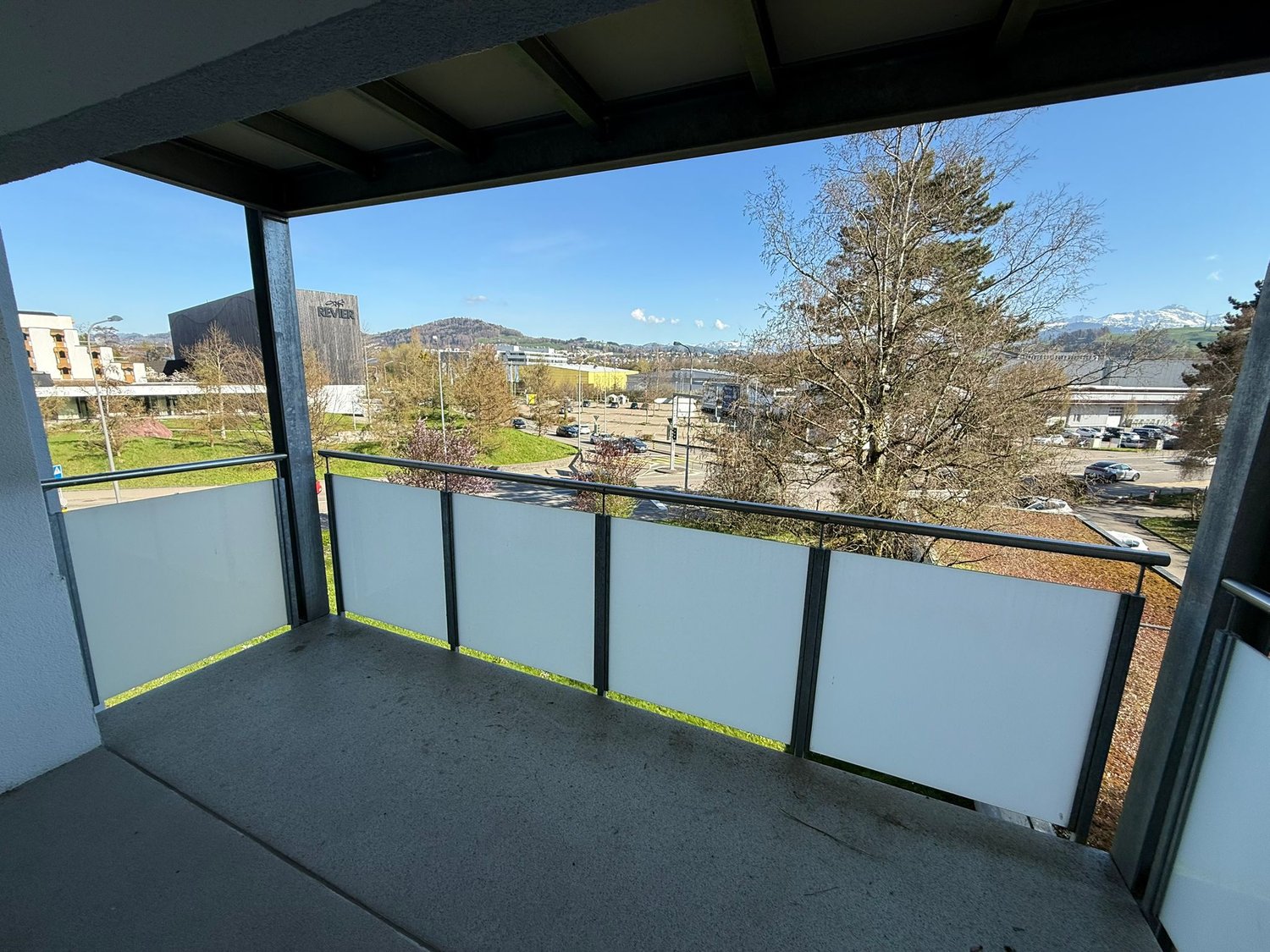 Balcony with glass railing, concrete floor, view of the city and mountains