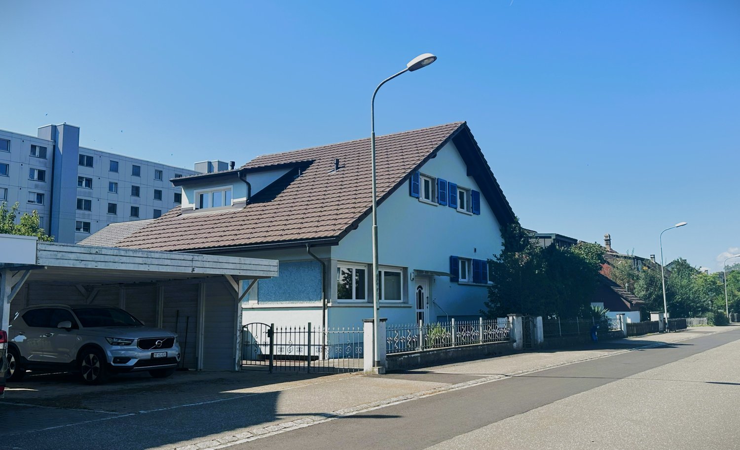 2 story house with brown roof, white walls, blue shutters, metal fence, car parked in garage