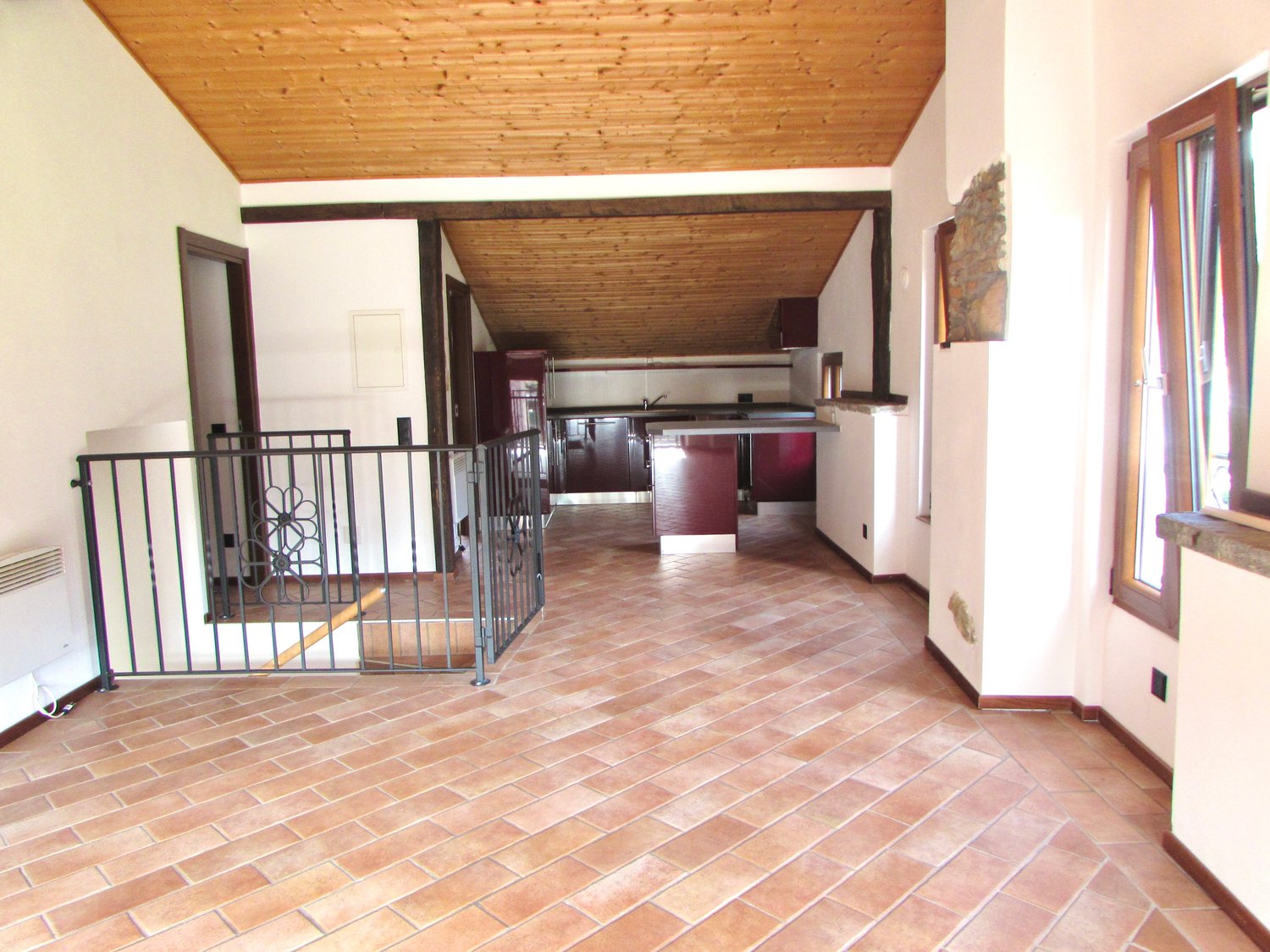 Large open space, wooden ceiling, tiled floor, kitchen area, glass window, metal railing