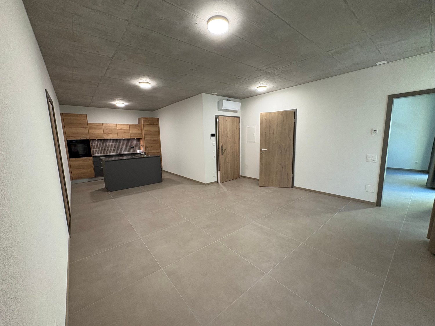 Large open space, kitchen area with island and cabinets, ceiling lamps, open doorways, large windows, tiled floor