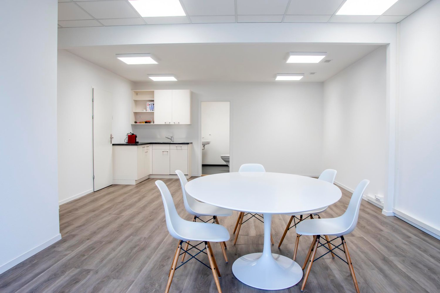 modern dining room with white round table, white chairs, light hardwood floors, modern kitchen, and built-in white cabinetry
