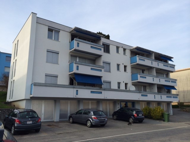 3-story apartment building with white and blue exterior, balconies, and parking spaces in front