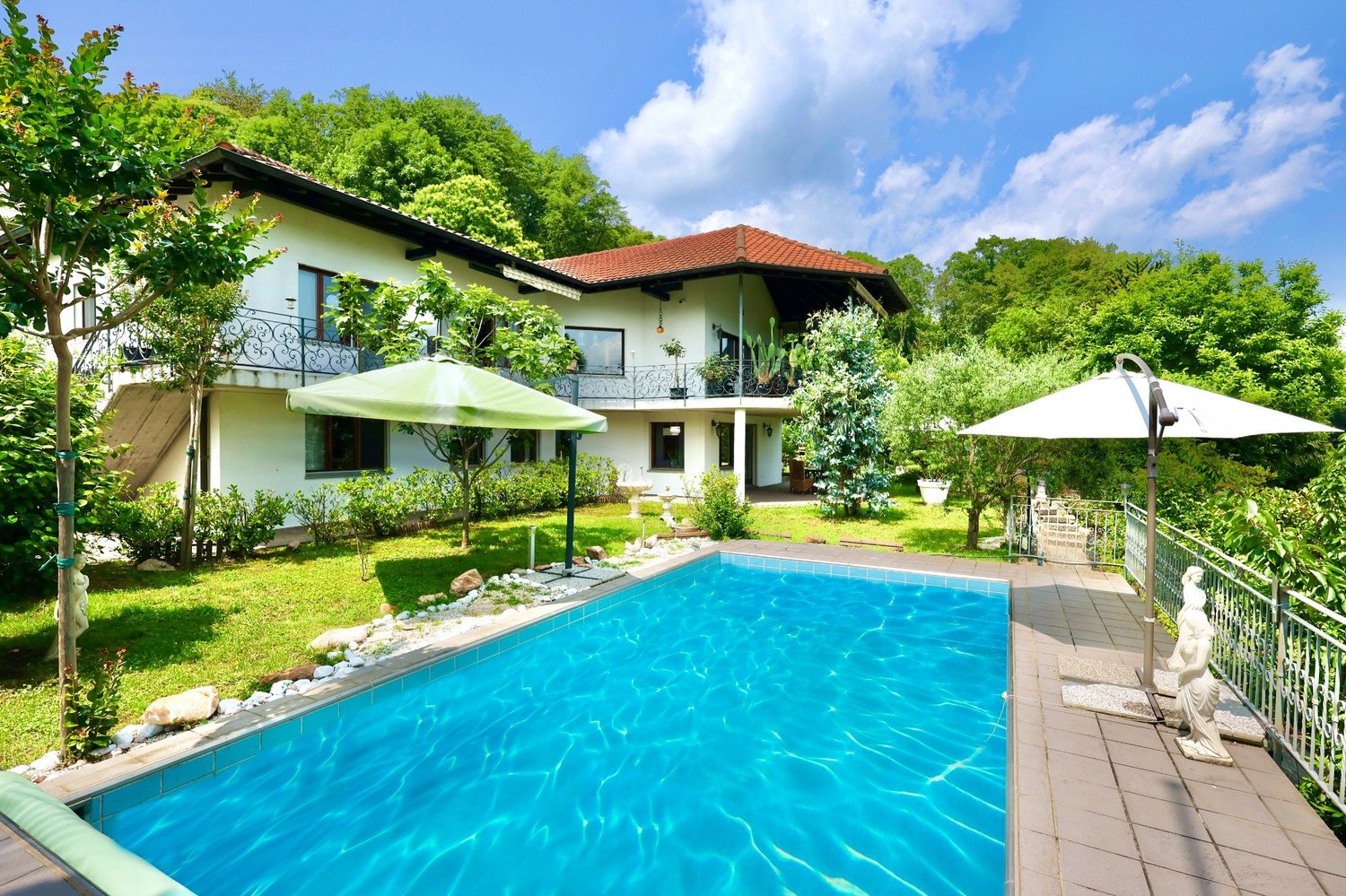 2-story villa, white exterior, red roof, large pool, patio, fence, trees, umbrellas, stairs