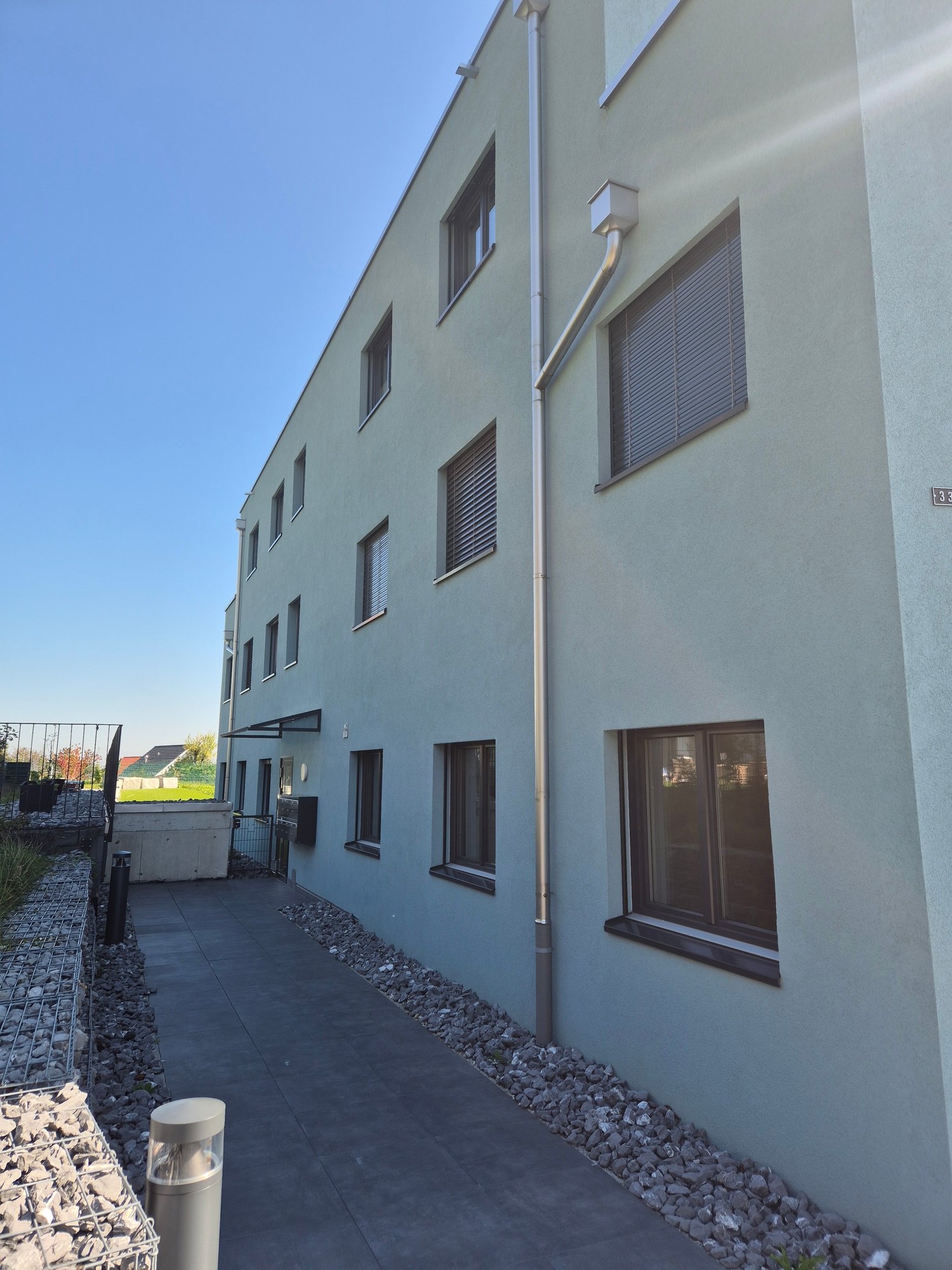 Three-story building, white exterior, multiple windows, entrance, parking area