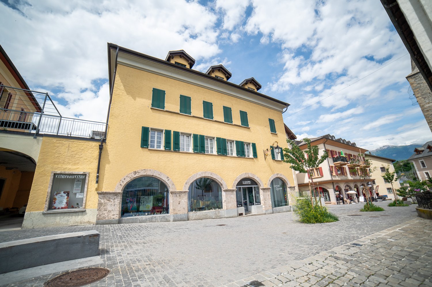 yellow facade, green shutters, arched windows, stone street, storefronts