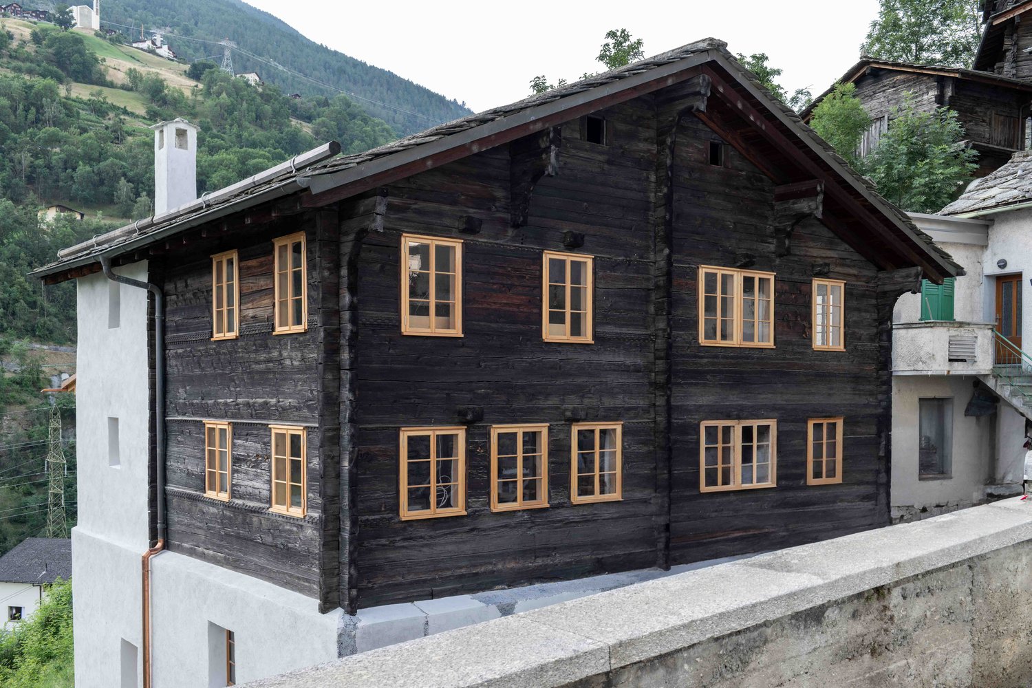 Traditional wooden chalet with yellow-framed windows, slate roof, chimney, mountain view