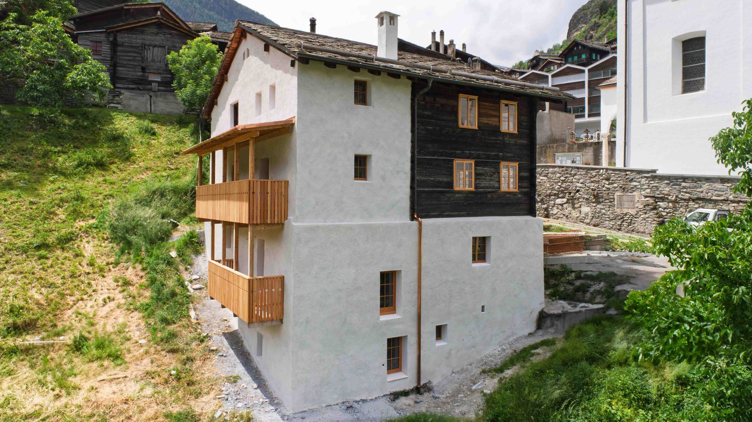 Modern design, white walls, black accents, terracotta roof, wooden balconies, large windows, situated on a hillside with a sloped terrain