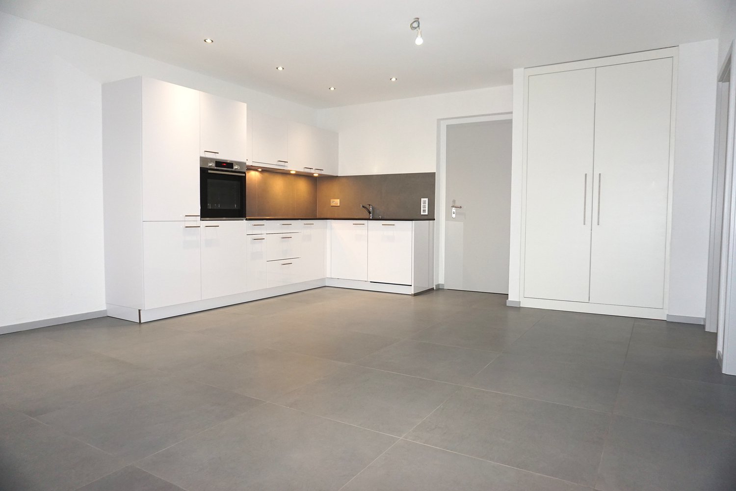 All white kitchen, tiled floor, integrated oven, dishwasher, sink, ample storage space, grey tiles