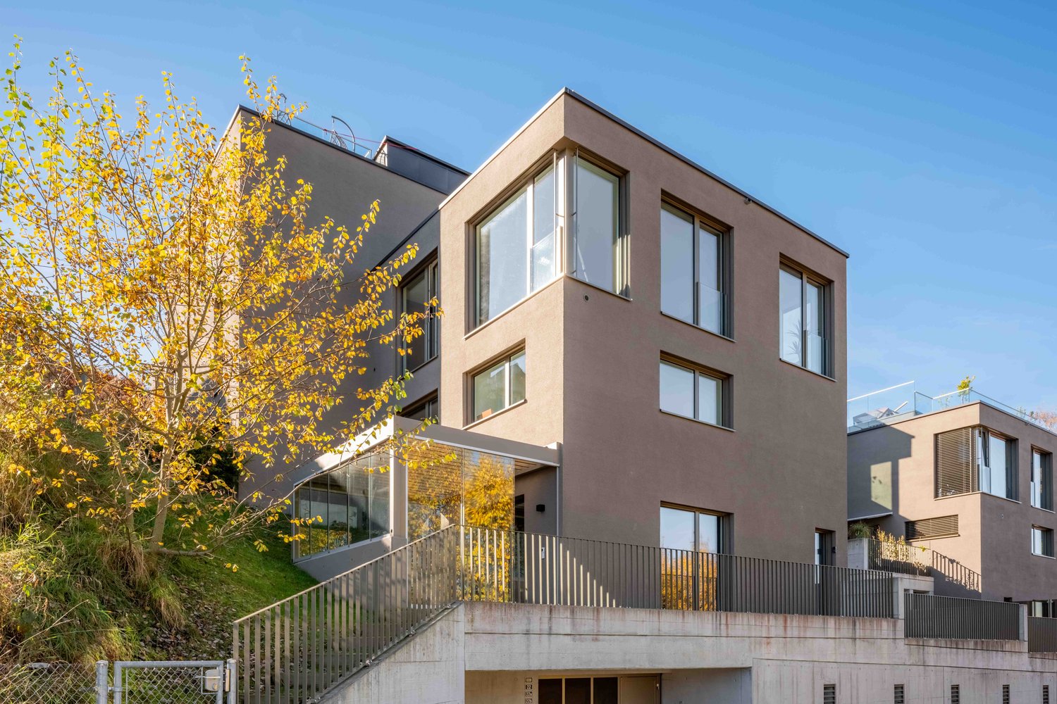 modern house, raised ground floor, multiple glass windows, balconies, sloped entrance