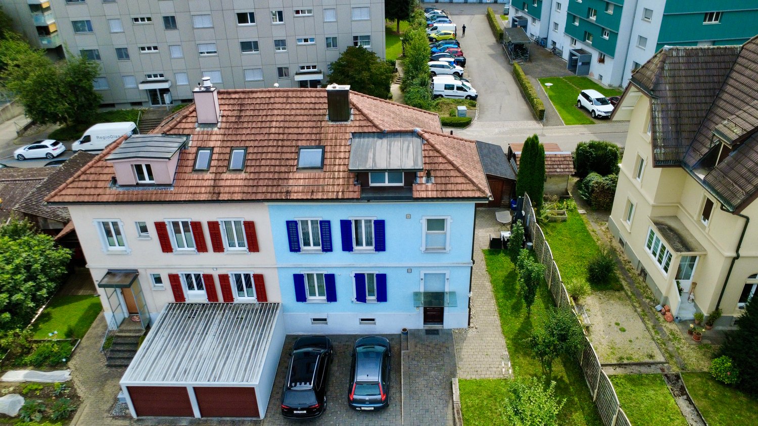 2 story house, red roof, blue walls, windows with red and blue shutters, garage, parking for 3 cars