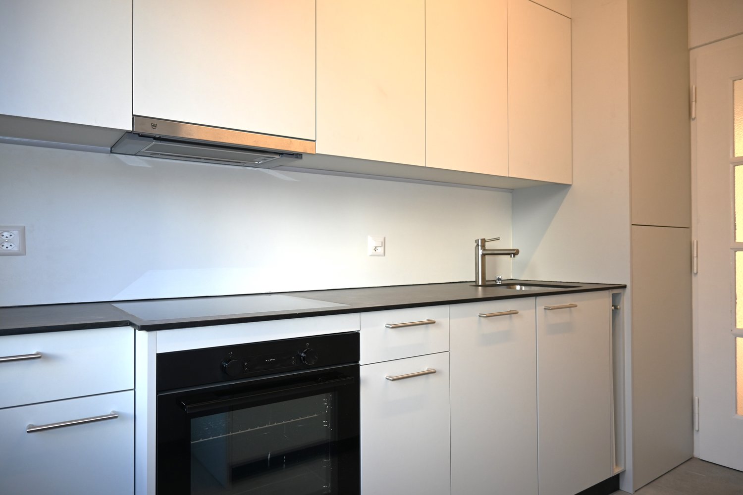 white cabinetry, black countertops, oven and stove, sink, faucet, power outlet, glass door