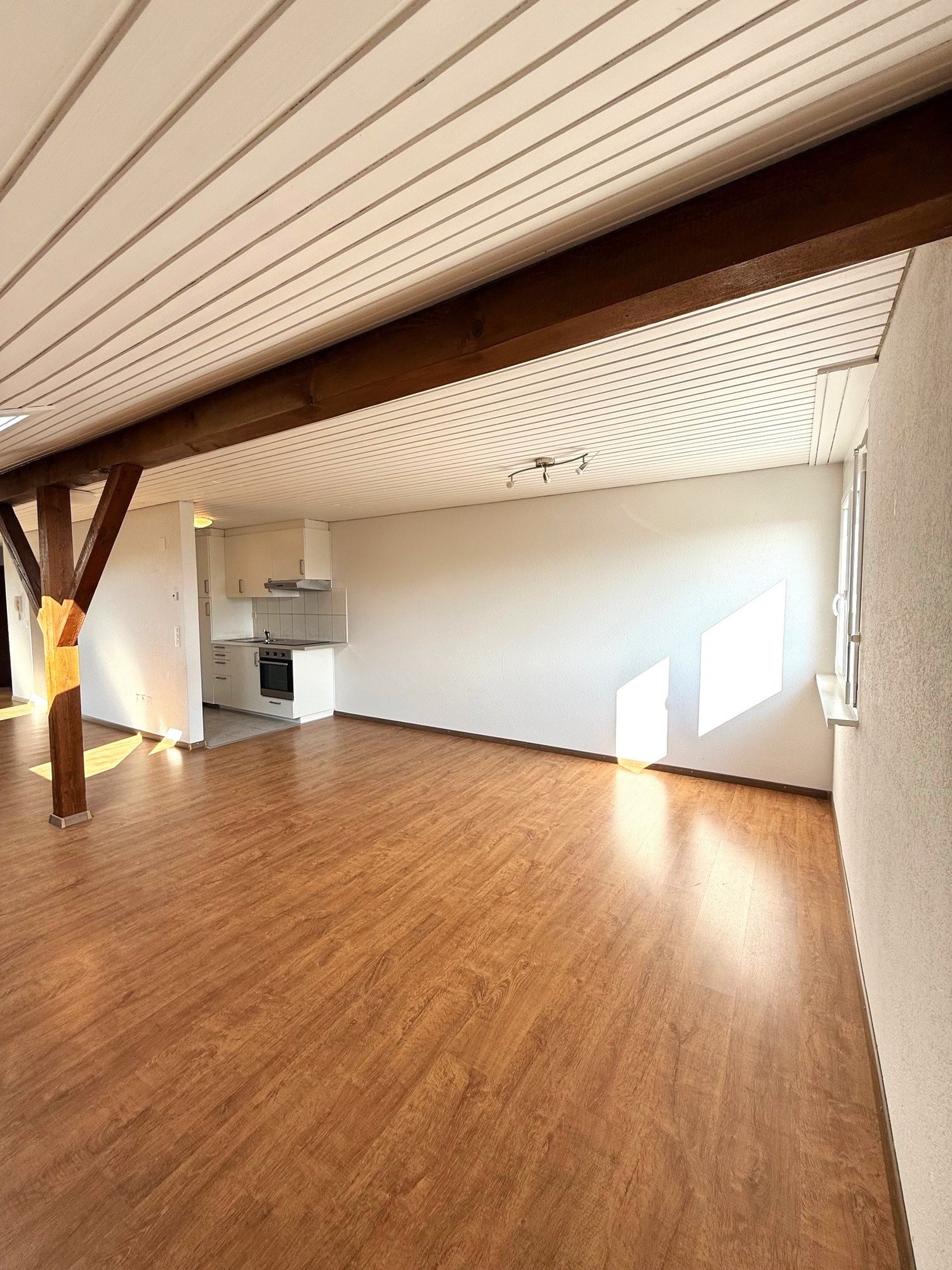 empty room, hardwood floors, wooden ceiling beams, white walls, kitchen, appliances, large windows