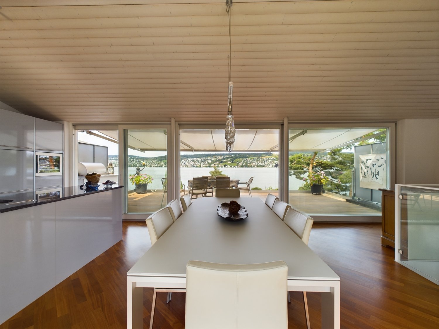 large dining room with wooden floors, large windows, outdoor dining table, kitchen counter, glass walls